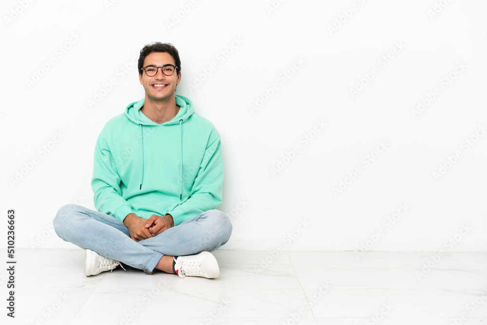 Caucasian handsome man sitting on the floor with glasses and happy