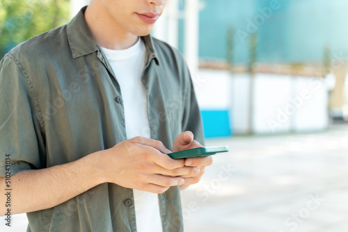 Man wearing casual clothes standing at the street and looking at his smartphone with smile