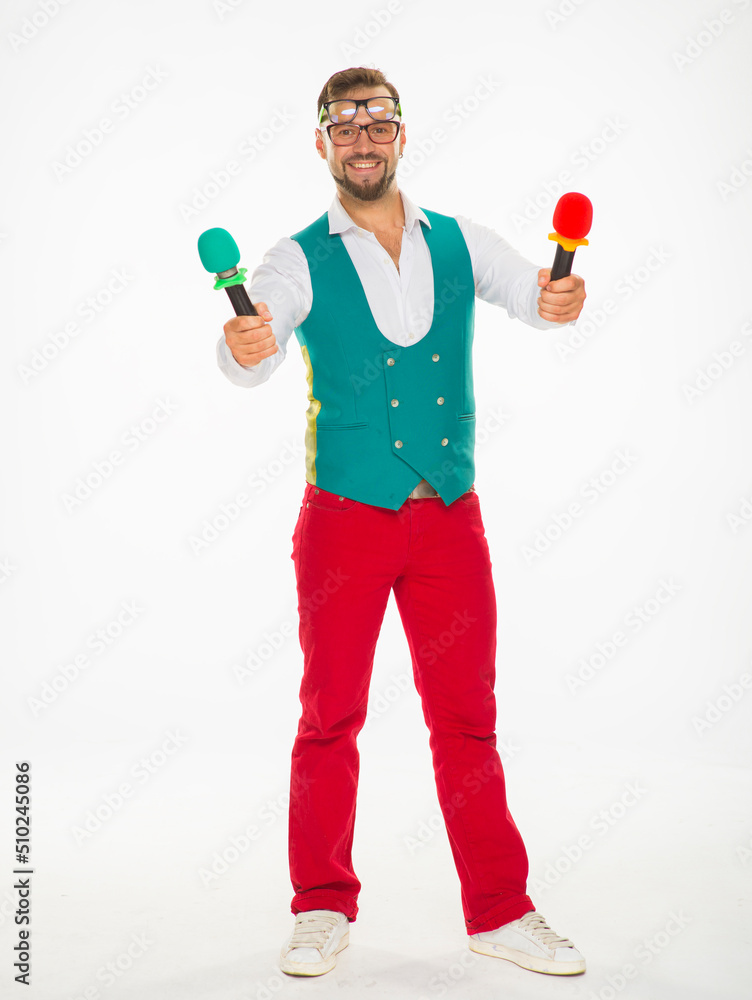 the guy with the microphone is smiling. a cheerful guy with two microphones in his hands and two pairs of glasses on his face poses funny in red trousers and a vest on a white isolated background the guy with the microphone is smiling. a cheerful guy with two microphones in his hands and two pairs of glasses on his face poses funny in red trousers and a vest on a white isolated background