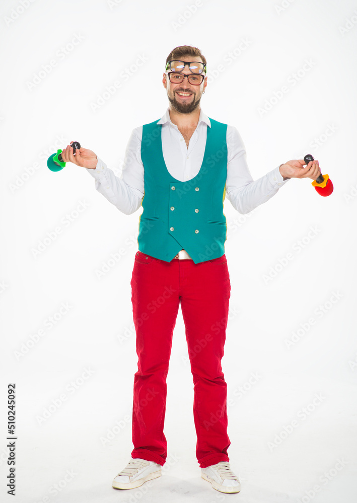 the guy with the microphone is smiling. a cheerful guy with two microphones in his hands and two pairs of glasses on his face poses funny in red trousers and a vest on a white isolated background the guy with the microphone is smiling. a cheerful guy with two microphones in his hands and two pairs of glasses on his face poses funny in red trousers and a vest on a white isolated background