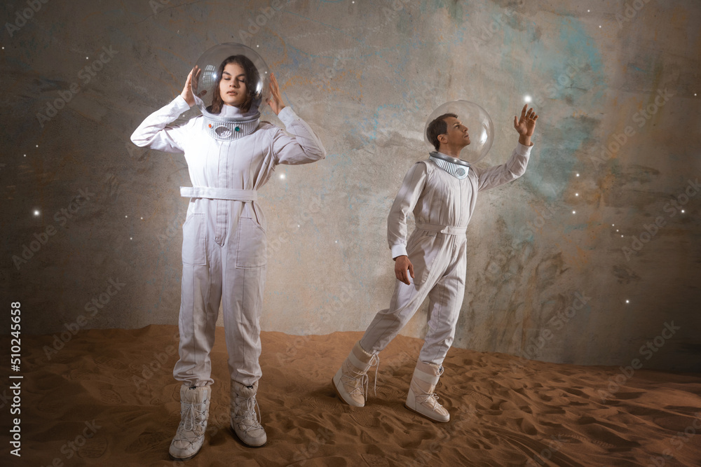 a man and a woman in white futuristic spacesuits explore the planet, astronauts in an empty colony on the sand, a holographic star map on the background a man and a woman in white futuristic spacesuits explore the planet, astronauts in an empty colony on the sand, a holographic star map on the background
