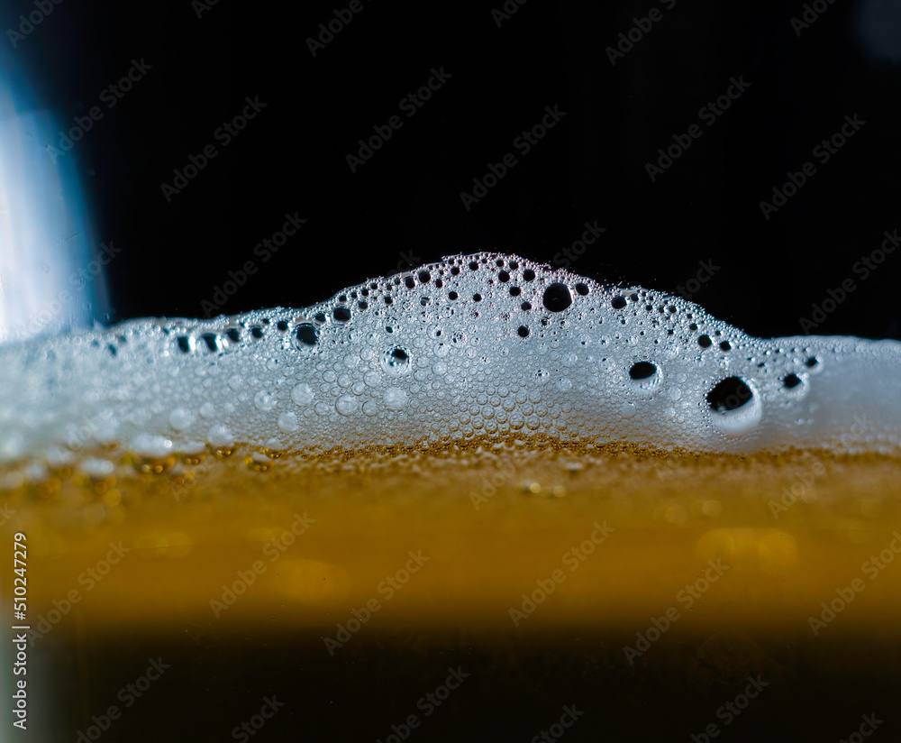 A closeup of dark beer in a cup with bubble suds at the top, foam formed on top of a alcoholic beverage.