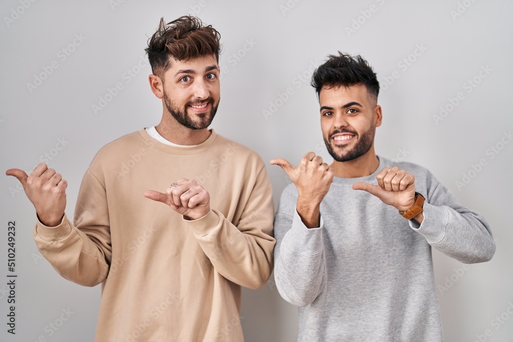 Young homosexual couple standing over white background pointing to the back behind with hand and thumbs up, smiling confident Young homosexual couple standing over white background pointing to the back behind with hand and thumbs up, smiling confident