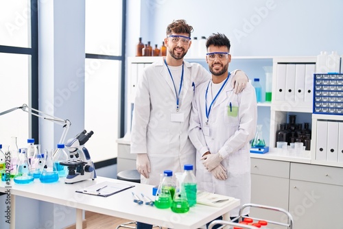 Young couple wearing scientist uniform hugging each other at laboratory