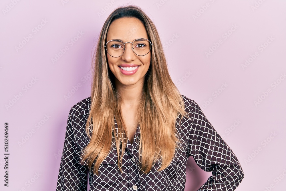 Obraz premium Beautiful hispanic woman wearing casual clothes and glasses looking positive and happy standing and smiling with a confident smile showing teeth