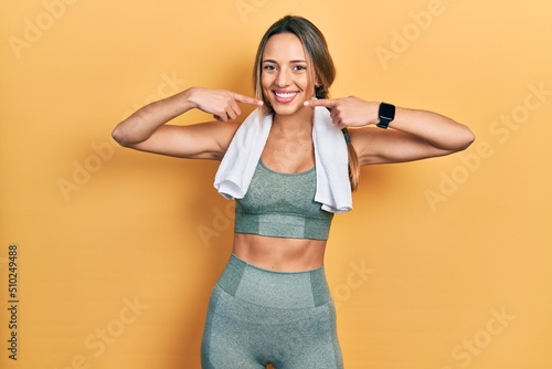 Beautiful hispanic woman wearing sportswear and towel smiling cheerful showing and pointing with fingers teeth and mouth. dental health concept.