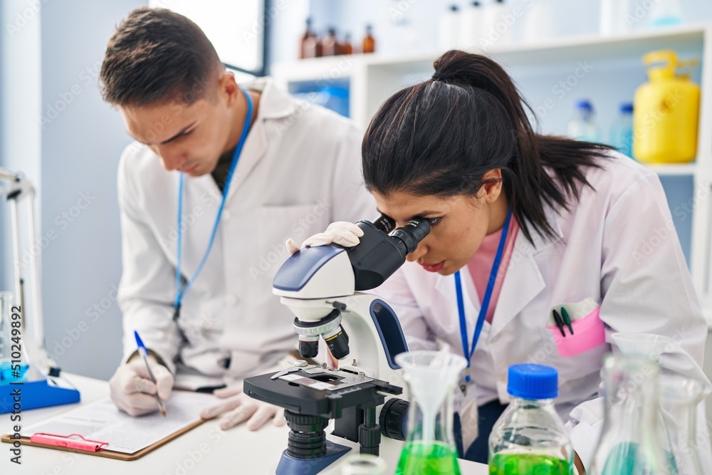 Man and woman scientists partners using microscope working at laboratory Man and woman scientists partners using microscope working at laboratory