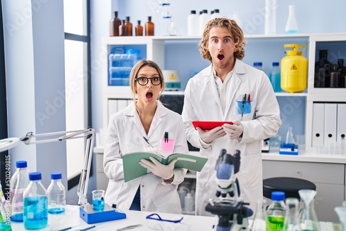 Two people working at scientist laboratory afraid and shocked with surprise and amazed expression  fear and excited face.