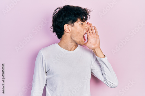 Handsome hipster young man wearing casual white shirt shouting and screaming loud to side with hand on mouth. communication concept. © Krakenimages.com