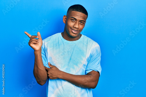 Young black man wearing tye die t shirt smiling happy pointing with hand and finger to the side
