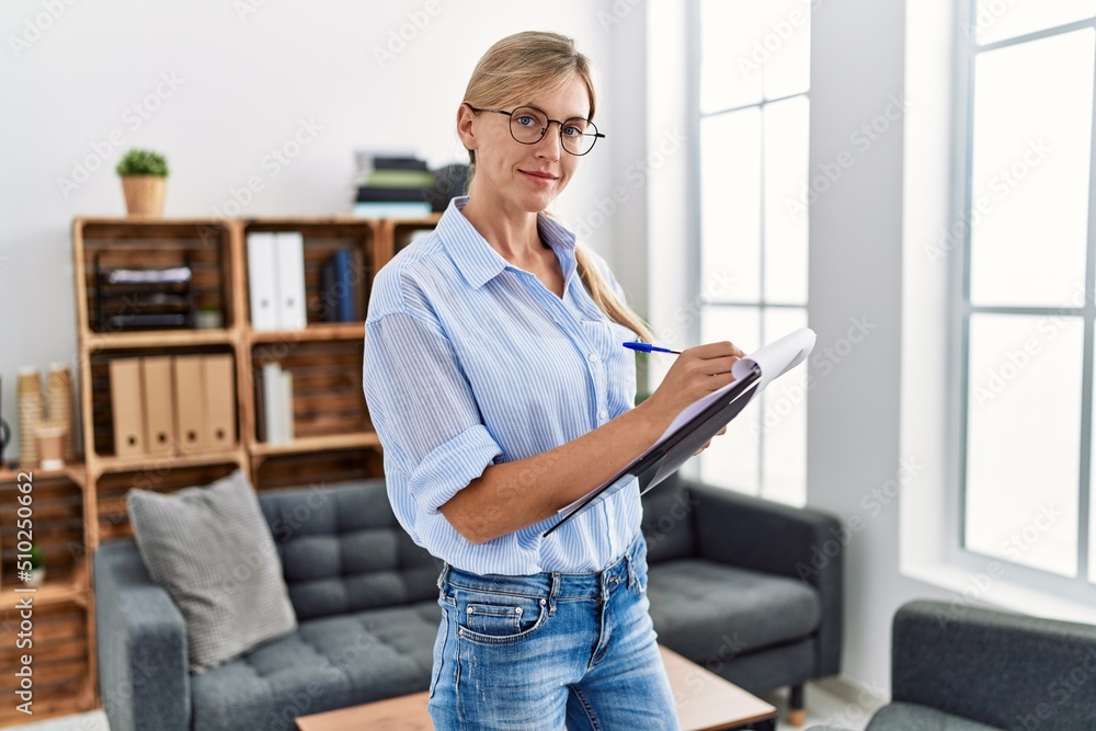 Young blonde woman psychologist writing on clipboard standing at clinic Young blonde woman psychologist writing on clipboard standing at clinic