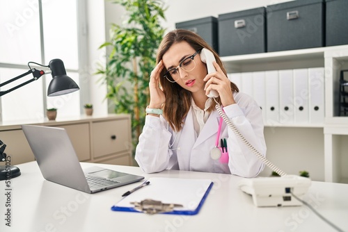 Young woman wearing doctor uniform stressed talking on the telephone at clinic