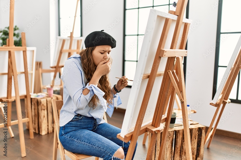 Obraz premium Young hispanic artist woman painting on canvas at art studio feeling unwell and coughing as symptom for cold or bronchitis. health care concept.
