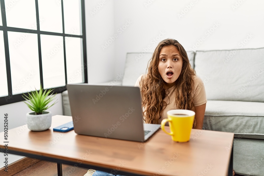 Beautiful hispanic woman using computer laptop at home scared and amazed with open mouth for surprise, disbelief face Beautiful hispanic woman using computer laptop at home scared and amazed with open mouth for surprise, disbelief face