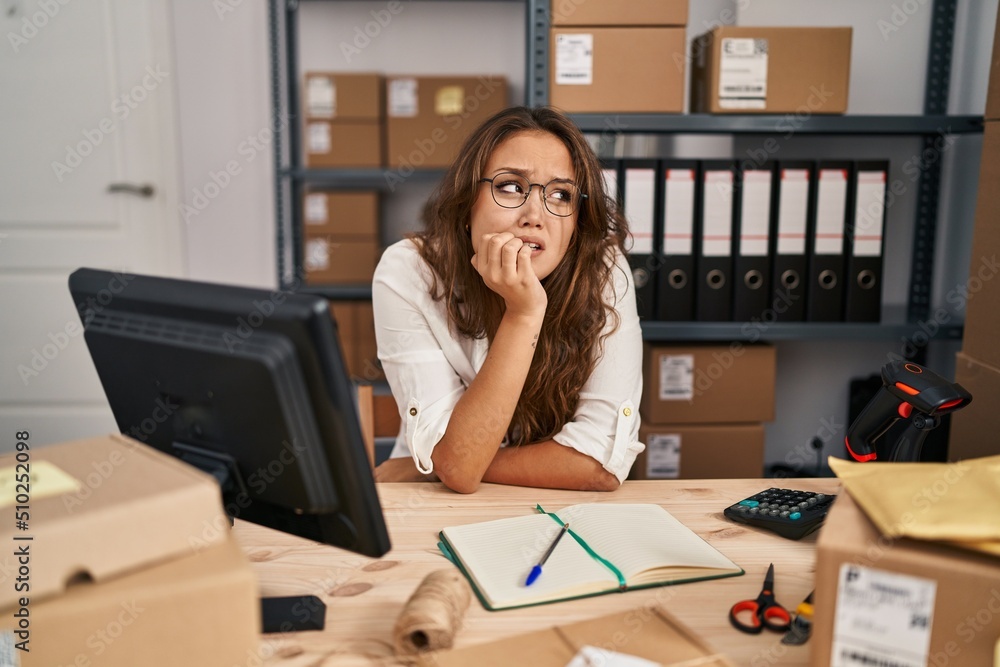 Young hispanic woman working at small business ecommerce looking stressed and nervous with hands on mouth biting nails. anxiety problem. Young hispanic woman working at small business ecommerce looking stressed and nervous with hands on mouth biting nails. anxiety problem.