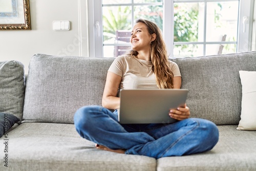 Young hispanic girl using laptop sitting on the sofa at home.