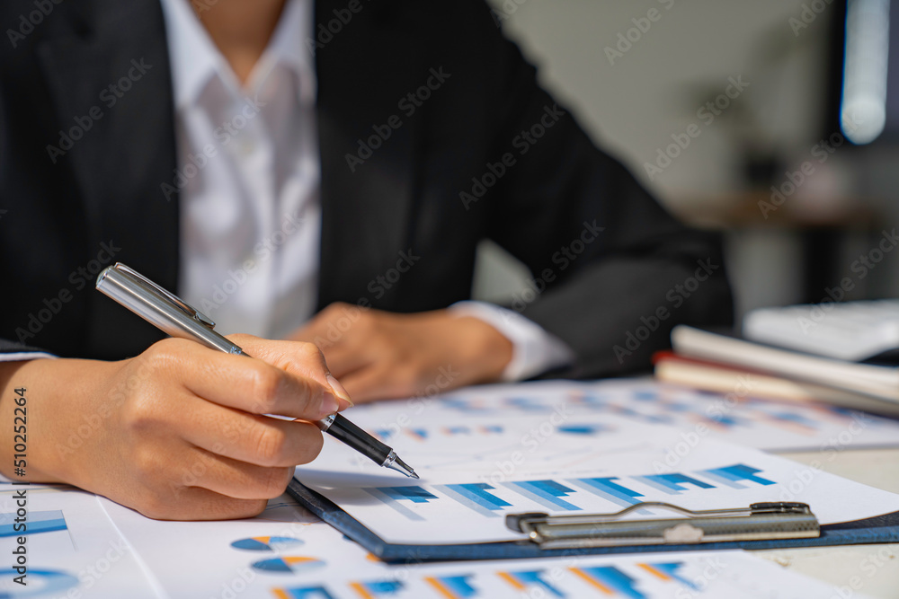 Businesswoman hold graph pens and use a calculator for the company's improvement plan. Businesswoman hold graph pens and use a calculator for the company's improvement plan.
