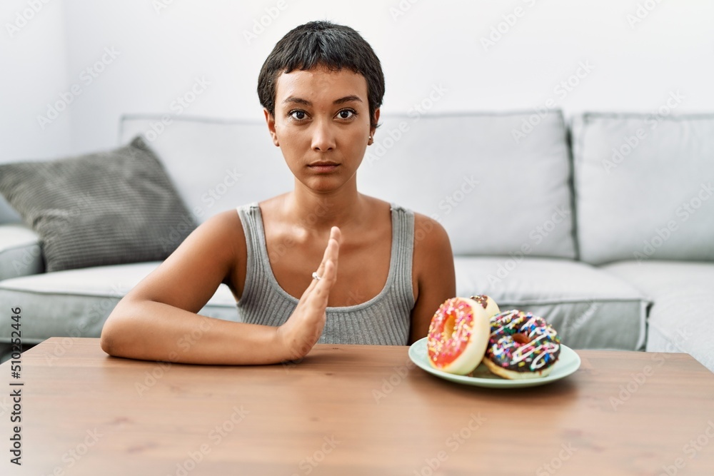 Young hispanic woman rejecting doughnut at home