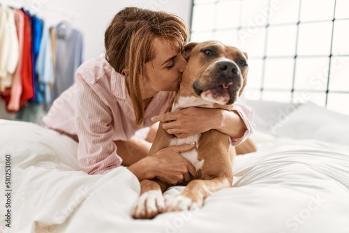 Young caucasian woman hugging and kissing dog lying on bed at bedroom