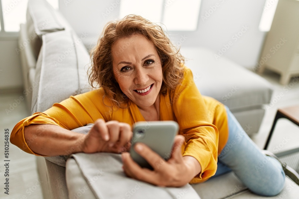 Middle age caucasian woman using smartphone sitting on the sofa at home. Middle age caucasian woman using smartphone sitting on the sofa at home.
