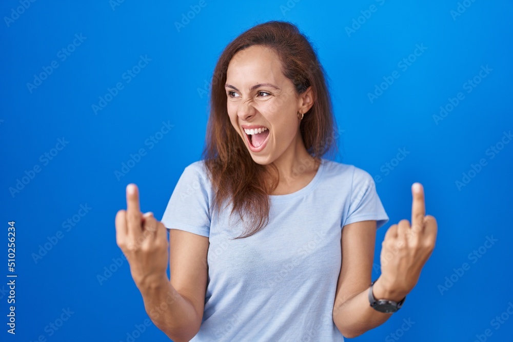 Brunette woman standing over blue background showing middle finger doing fuck you bad expression, provocation and rude attitude. screaming excited Brunette woman standing over blue background showing middle finger doing fuck you bad expression, provocation and rude attitude. screaming excited