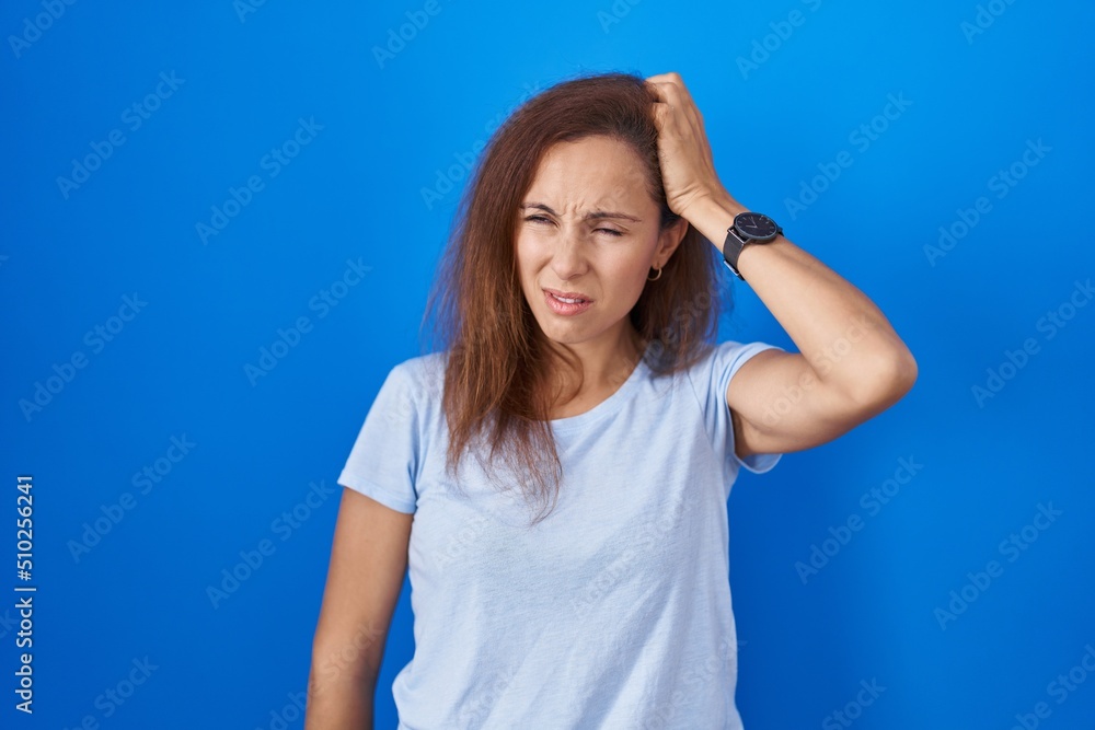 Brunette woman standing over blue background confuse and wondering about question. uncertain with doubt, thinking with hand on head. pensive concept. Brunette woman standing over blue background confuse and wondering about question. uncertain with doubt, thinking with hand on head. pensive concept.