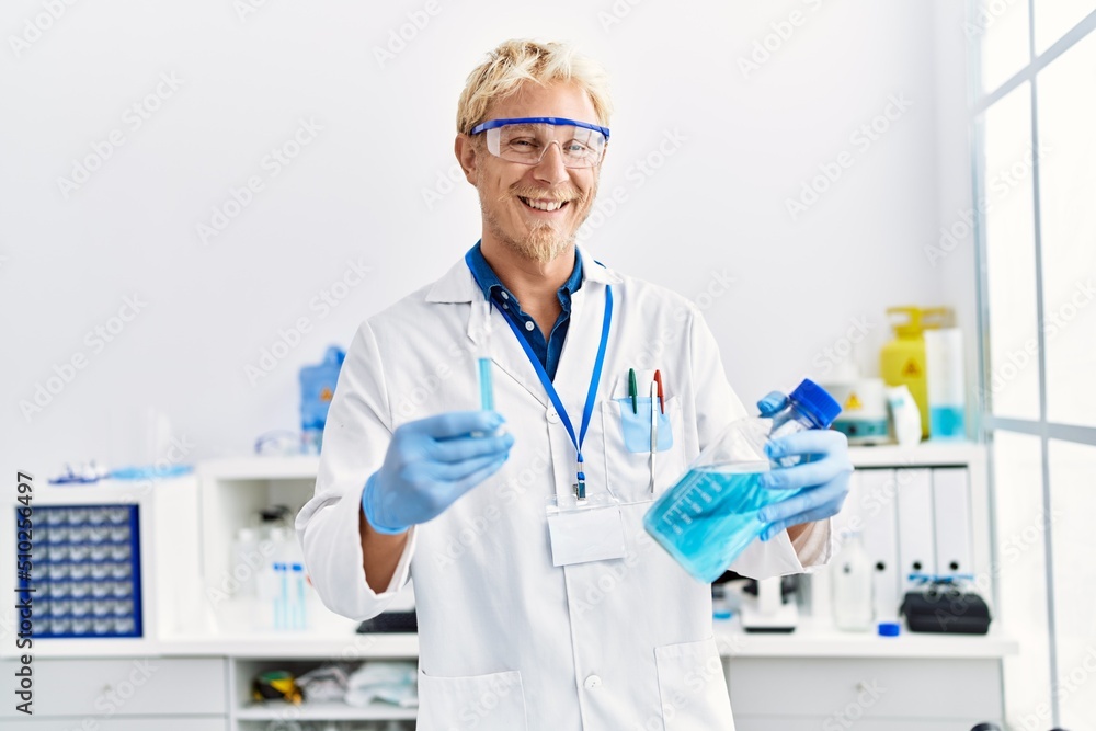 Young caucasian man wearing scientist uniform holding test tube at laboratory Young caucasian man wearing scientist uniform holding test tube at laboratory