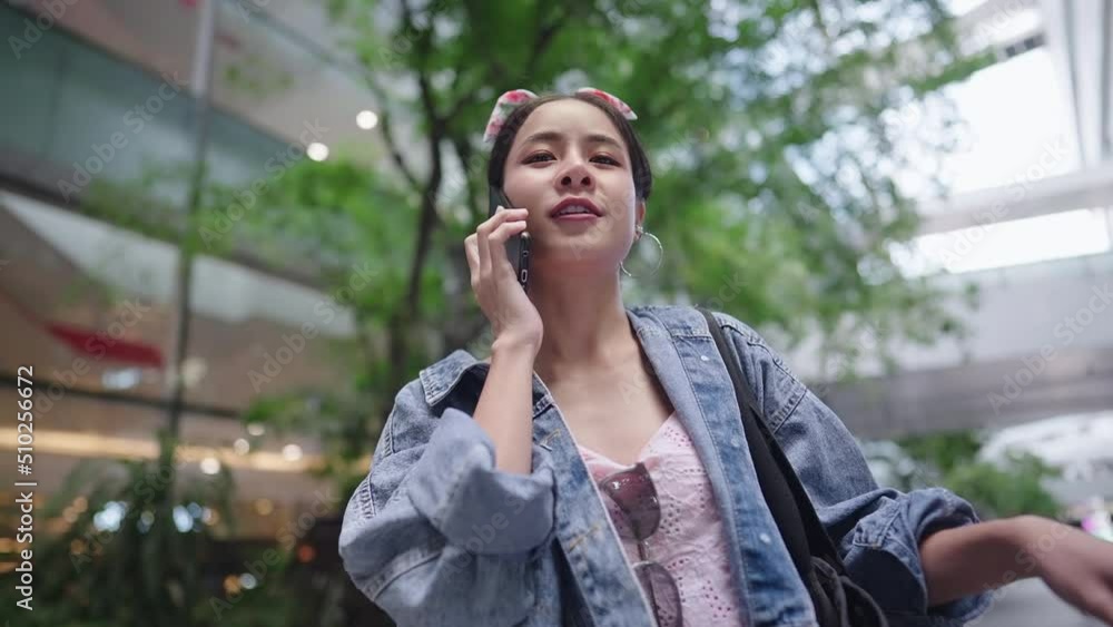 Young stylish Asian female talking on the phone while waiting for friends at the shopping mall, 5g technology for urban living, shopaholic weekend meet up, arrived on time but her friends are late Young stylish Asian female talking on the phone while waiting for friends at the shopping mall, 5g technology for urban living, shopaholic weekend meet up, arrived on time but her friends are late