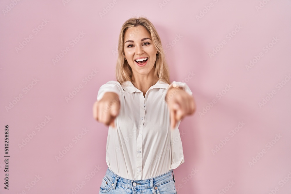 Young caucasian woman wearing casual white shirt over pink background pointing to you and the camera with fingers, smiling positive and cheerful Young caucasian woman wearing casual white shirt over pink background pointing to you and the camera with fingers, smiling positive and cheerful
