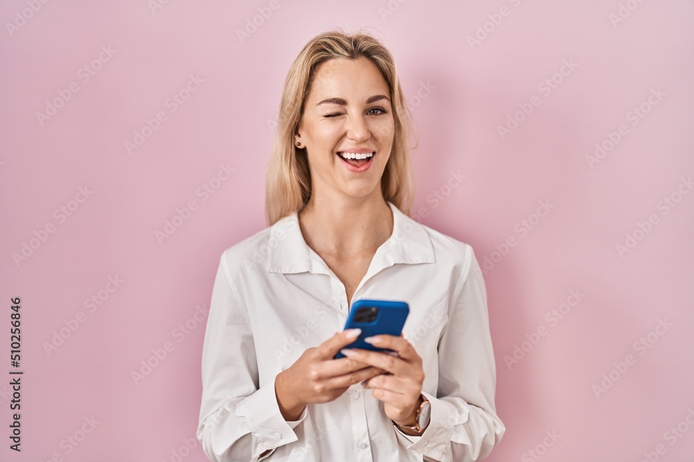 Young caucasian woman using smartphone typing message winking looking at the camera with sexy expression, cheerful and happy face. Young caucasian woman using smartphone typing message winking looking at the camera with sexy expression, cheerful and happy face.