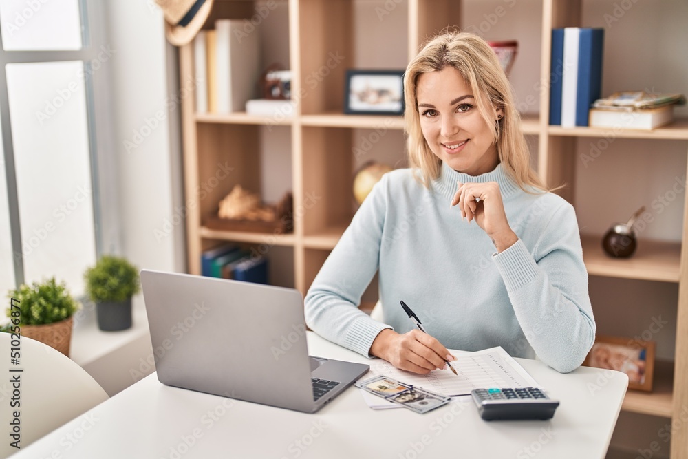 Young blonde woman sitting on table working at home Young blonde woman sitting on table working at home