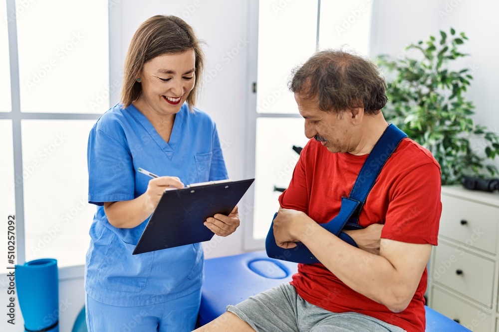Middle age man and woman wearing physiotherapy uniform having rehab session at physiotherapy clinic Middle age man and woman wearing physiotherapy uniform having rehab session at physiotherapy clinic