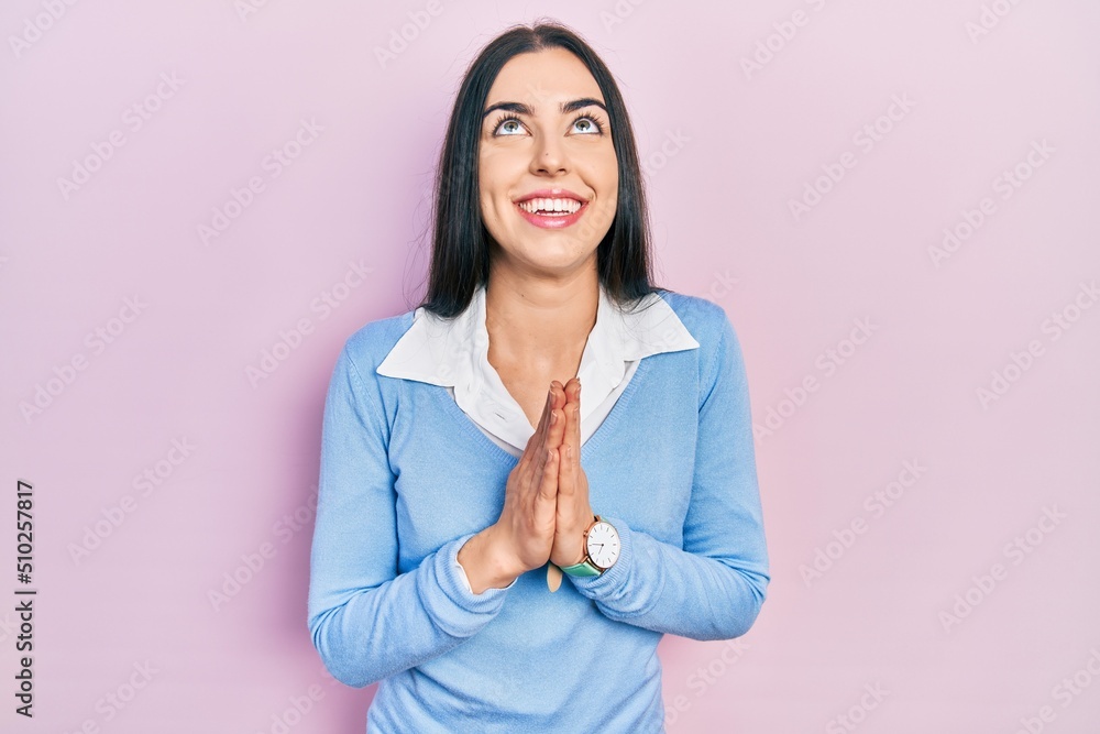 Beautiful woman with blue eyes standing over pink background begging and praying with hands together with hope expression on face very emotional and worried. begging. Beautiful woman with blue eyes standing over pink background begging and praying with hands together with hope expression on face very emotional and worried. begging.