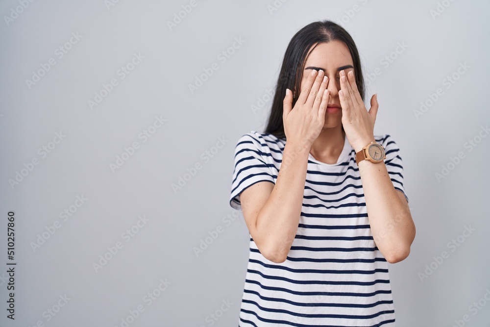 Young brunette woman wearing striped t shirt rubbing eyes for fatigue and headache, sleepy and tired expression. vision problem Young brunette woman wearing striped t shirt rubbing eyes for fatigue and headache, sleepy and tired expression. vision problem