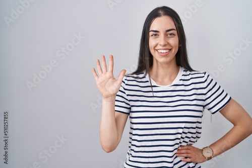 Young brunette woman wearing striped t shirt showing and pointing up with fingers number five while smiling confident and happy.