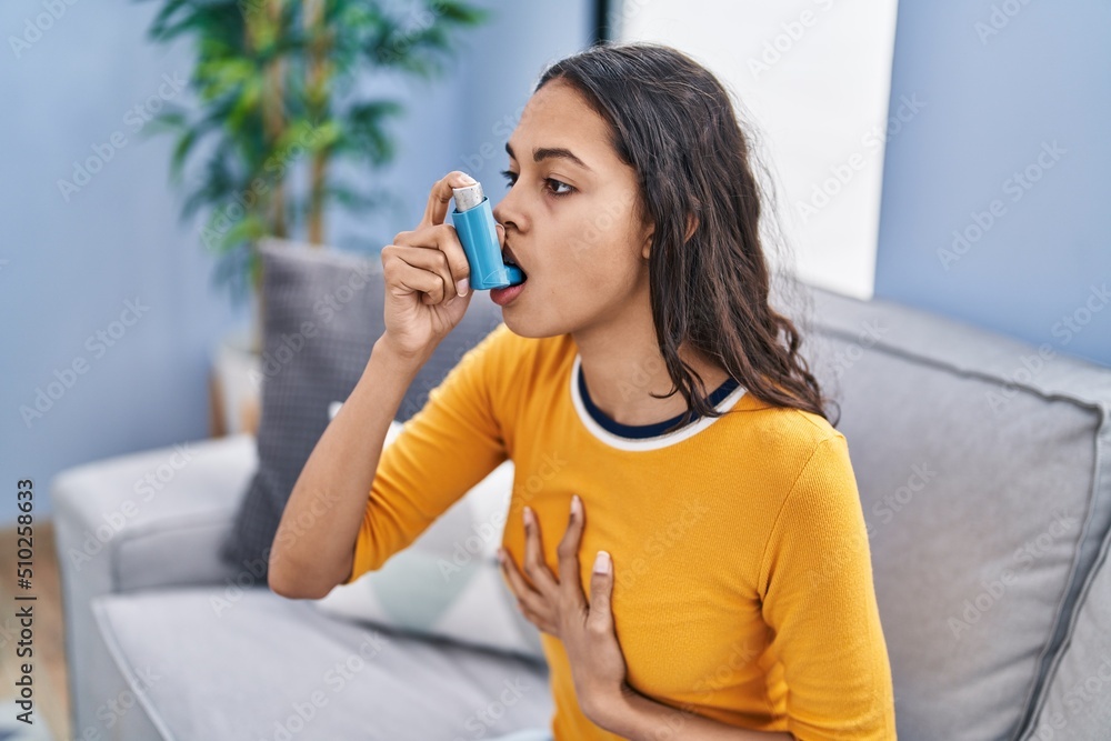 Young african american woman using inhaler sitting on sofa at home Young african american woman using inhaler sitting on sofa at home