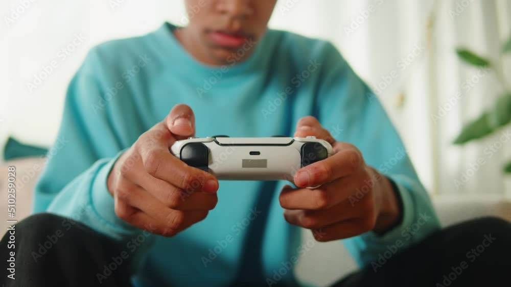 African American man playing video games on modern console. Happy young guy sitting on sofa in living room, cheerful teenager using white gamepad, enjoying AR 3D game. African American man playing video games on modern console. Happy young guy sitting on sofa in living room, cheerful teenager using white gamepad, enjoying AR 3D game.