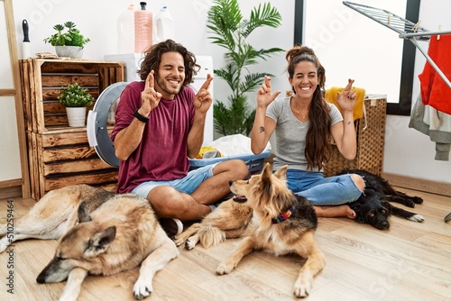 Wall Mural Young hispanic couple doing laundry with dogs gesturing finger crossed smiling with hope and eyes closed