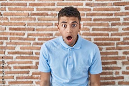 Brazilian young man standing over brick wall afraid and shocked with surprise and amazed expression, fear and excited face.