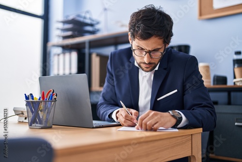 Fotobehang Young hispanic man business worker using laptop write on document at office