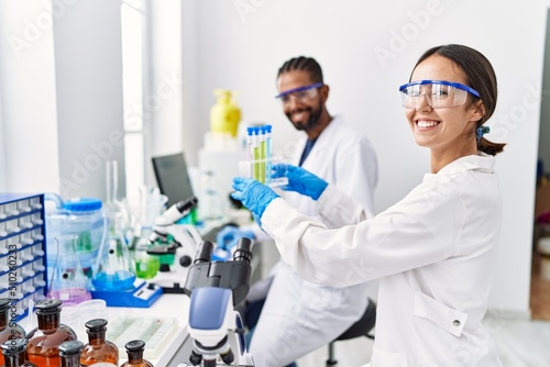 Man and woman scientist partners smiling confident holding test tube at laboratory