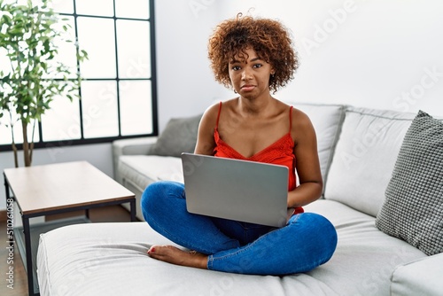Young african american woman sitting on the sofa at home using laptop depressed and worry for distress, crying angry and afraid. sad expression.