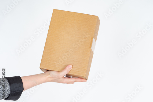 Cardboard box in hand. Concept of postal parcels. Cardboard package without inscriptions. Place for brand or advertisement on box. Girl hand with small box. Cardboard parcel on light background © Grispb