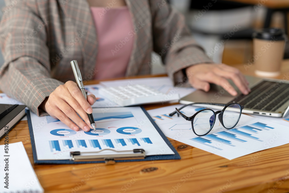 Business woman hand uses a laptop to work on charts and graphs that show results. She uses the pen to point to the graph. Business woman hand uses a laptop to work on charts and graphs that show results. She uses the pen to point to the graph.