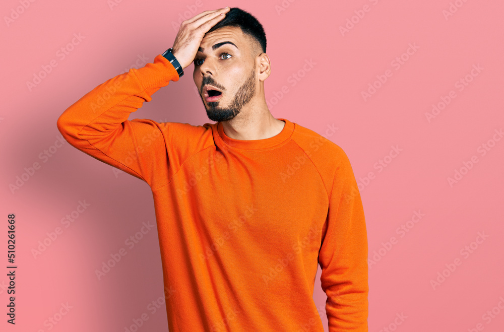 Young hispanic man with beard wearing casual orange sweater surprised with hand on head for mistake, remember error. forgot, bad memory concept. Young hispanic man with beard wearing casual orange sweater surprised with hand on head for mistake, remember error. forgot, bad memory concept.