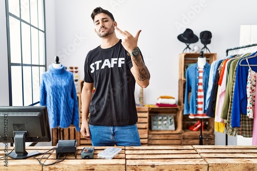 Young hispanic man working at retail boutique showing middle finger, impolite and rude fuck off expression photo