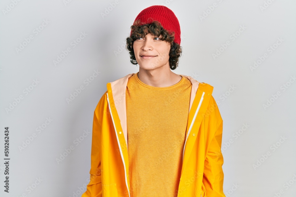 Handsome young man wearing yellow raincoat looking away to side with smile on face, natural expression. laughing confident. Handsome young man wearing yellow raincoat looking away to side with smile on face, natural expression. laughing confident.