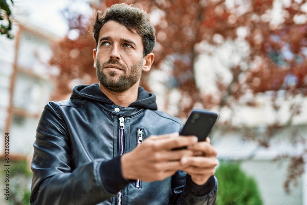 Handsome hispanic man with beard with serious face outdoors using smartphone Handsome hispanic man with beard with serious face outdoors using smartphone
