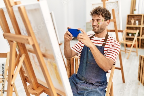 Young hispanic man make photo to draw using smartphone at art studio
