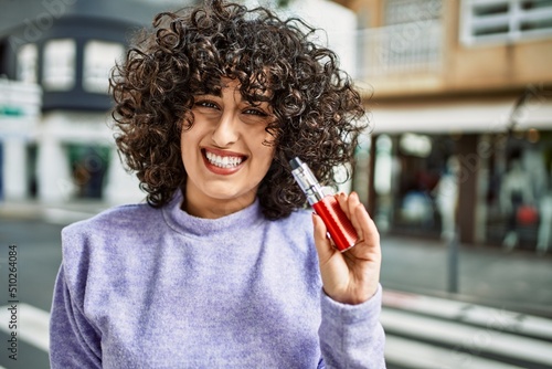 Young middle east woman smiling confident holding electronic cigarette at street